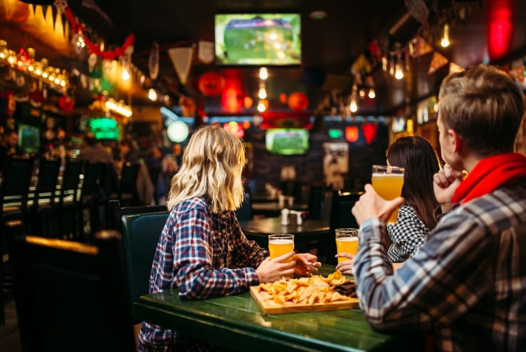 Friends watching game on TV screens at a lively sports bar with beer